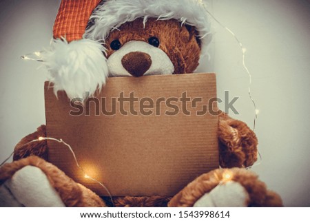 Christmas card with Teddy bear holding a place for text and other Christmas decor light garland. Toned photo, copy space.