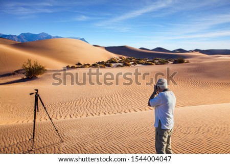Sunset in desert. Death Valley. USA. Gray-haired man - tourist in white T-shirt photographs magnificent landscape. Tripod standing by. Concept of active and photo tourism