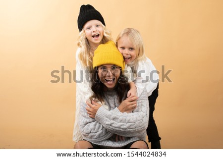 A young and energetic mother hugs and kisses her children on an orange background