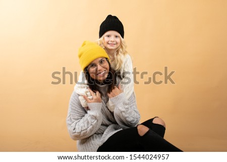 A young and energetic mother hugs and kisses her daughter on an orange background