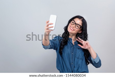 Happy young woman taking a selfie on a gray background