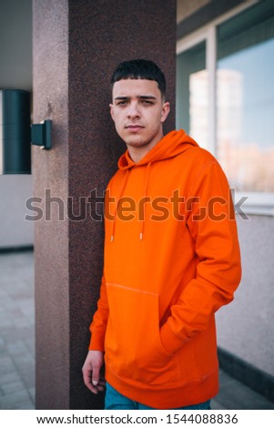 City portrait of handsome hipster guy wearing orange blank hoodie or hoody with space for your logo or design. Mockup for print