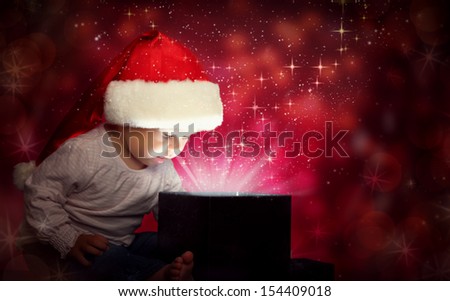 happy baby child girl in Christmas hat opening a magic gift box in the dark