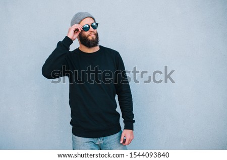 City portrait of handsome hipster guy with beard wearing black blank hoody or sweatshirt and hat with space for your logo or design. Mockup for print