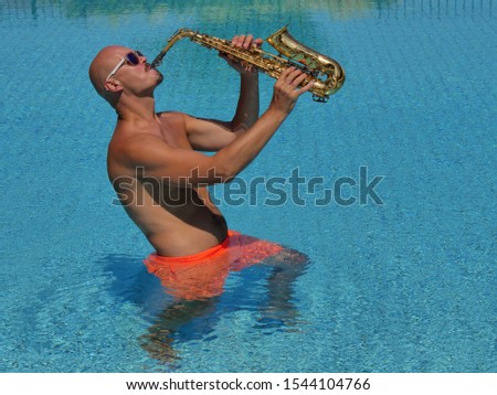 Saxophone player in orange swimming trunks stands waist-deep in water and plays the golden alto saxophone