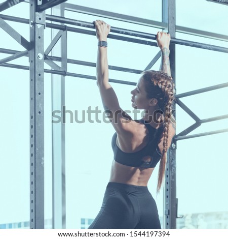 Portrait of beautiful athletic woman doing pull-up exercise, image with cold vintage toning