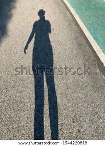 Shadow of a woman while she was walking running along the park during the summer time.