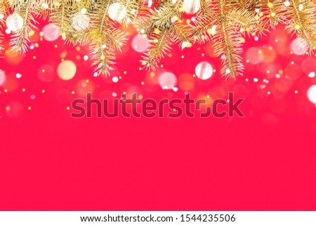 Festive composition with border of fluffy gold fir branches and golden confetti stars sparse on red background. Christmas lights bokeh. Top view, flat lay style, copy space for text.