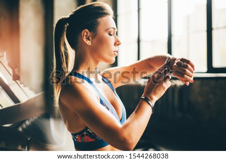 Sport woman looks at smart watch after training in gym. Healthy concept. Female after workout session checks results on watch.