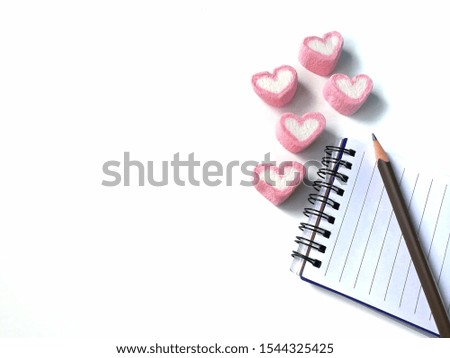 Pink hearts shaped marshmallow and a notebook with a pencil are placed on white background, Valentine day