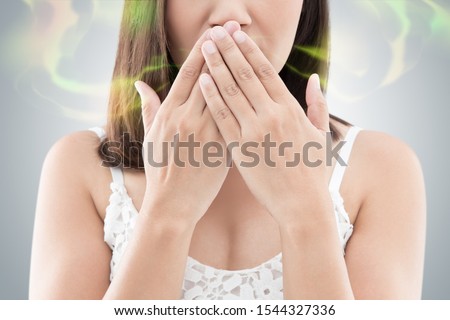 Asian woman in white wear close her mouth against gray background, Bad breath Royalty-Free Stock Photo #1544327336