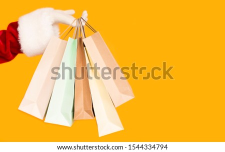 Merry Christmas. Santa holding Christmas shopping bags with presents over orange background, copy space