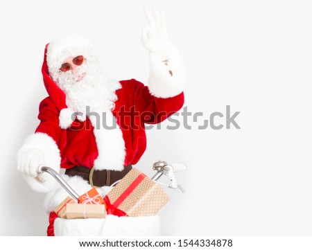 Happy Santa in sun glasses showing ok sign and riding a bike with presents, white background, copy space