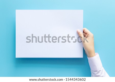 close up hands holding empty white blank letter paper size A4 for flyer or invitation mock up isolated on a blue background.