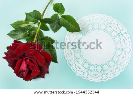 A red rose and a beautiful lace napkin lie on a blue background. Space for text.