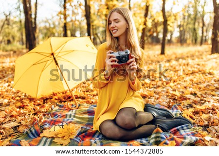 happy smiling young woman in autumn Park sitting on blanket posing with retro camera taking pictures enjoying warm autumn weather