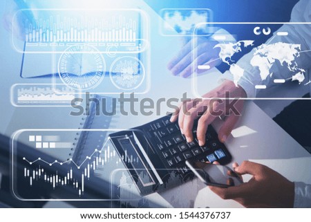 Hands of business people working together in office with double exposure of blurry infographic interface. Concept of big data and fintech. Toned image
