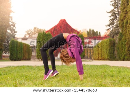 Little girl gymnast standing in arch pose outdoors in the autumn park smiling joyful