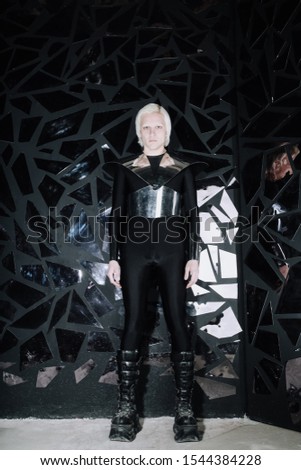 young blonde caucasian man standing in alien cosmos halloween costume and looking near the many mirrors and reflecting on black background