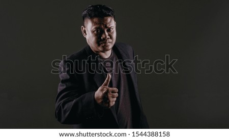 A man wearing a blazer show thumb up finger. Grey background and studio low light setup.