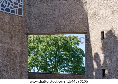 Close up detail of tree behind the rectangular hole of exterior sandstone concrete facade with abstract pattern ornament decorate on windows of brutalist architecture church in Cologne, Germany. 