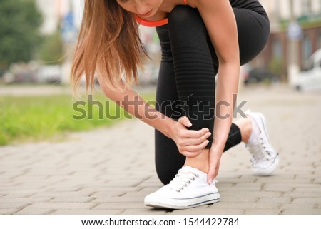 Young sporty woman suffering from pain in ankle outdoors