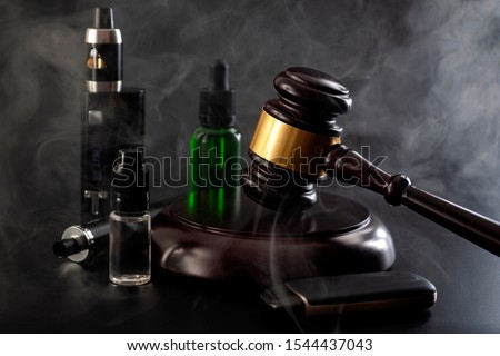 Legal act to restrict vaping, outlaw smoking electronic cigarettes and vape ban legislation conceptual idea with judge gavel, vape device, bottle of ejuice and some isolated on black background Royalty-Free Stock Photo #1544437043