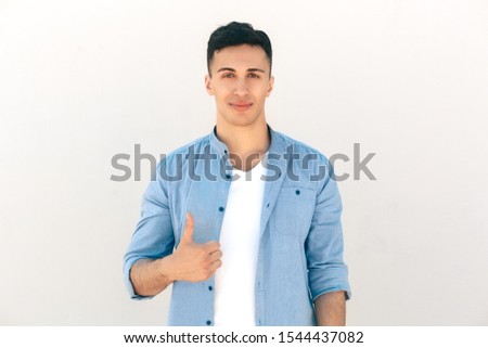 Stylish young man standing outdoors isolated on white background showing thumb up looking camera smiling satisfied