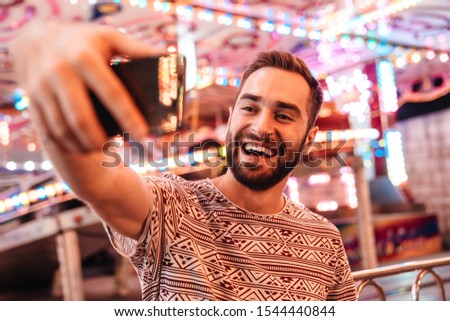 Photo of happy smiling man walking outdoors in amusement park take selfie by mobile phone.