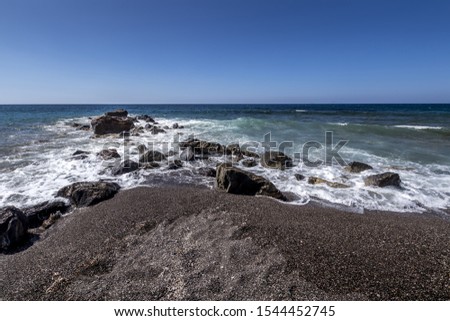 Sea surf on the beach with black volkanic sand and stones. Close-up. Abstract background. Vlihada, Santorini. Seascape.