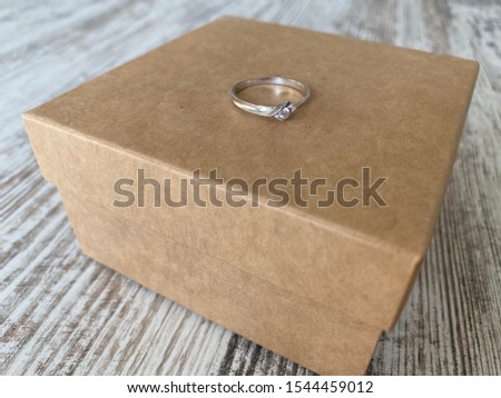 Kraft paper box with silver engagement ring with gemstone on it laying on shabby desk 