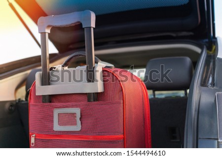 A red suitcase with a retractable handle is waiting to go on in the trunk of a black car. Moving luggage in auto. Use it for trip, holidays, vacation and outdoors lifestyle concept. Royalty-Free Stock Photo #1544494610