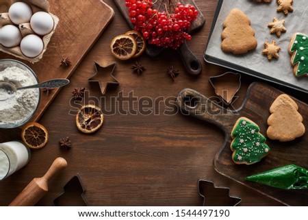 top view of glazed Christmas cookies near ingredients, dough molds and viburnum on wooden table