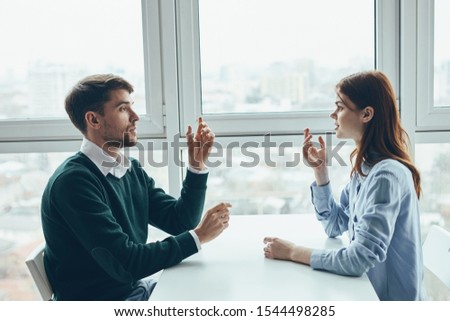 A man and a woman are talking at a table near the window