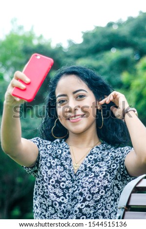 Portrait of a beautiful young woman dressed in a black and white shirt with flowers looking at the camera while taking a photo of herself. Concept of feminine beauty. Vertical image