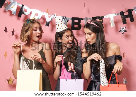 Image of delighted party girls in fancy dresses unpacking birthday gifts isolated over pink background