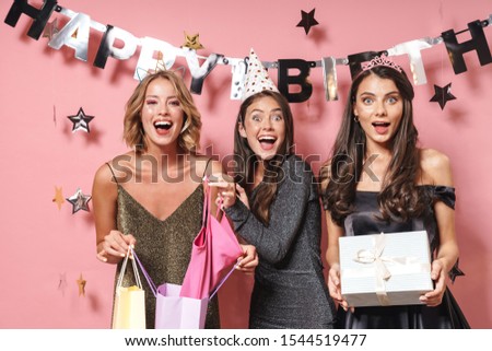 Image of gorgeous party girls in fancy dresses unpacking birthday gifts isolated over pink background