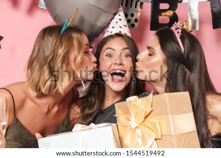 Image of alluring party girls in fancy dresses celebrating birthday with gift boxes isolated over pink background