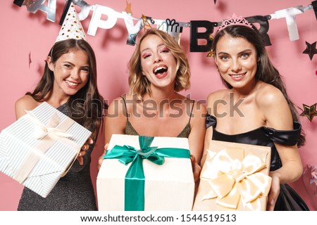 Image of seductive party girls in fancy dresses holding birthday gift boxes isolated over pink background