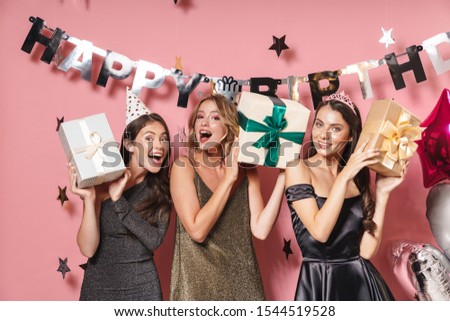Image of young party girls in fancy dresses holding birthday gift boxes isolated over pink background