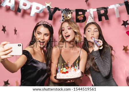 Image of adorable party girls taking selfie photo on smartphone and holding birthday cake with candles isolated over pink background