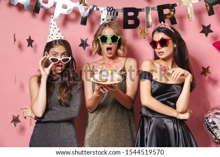 Image of adorable party girls in glamour sunglasses holding birthday cake with candles isolated over pink background