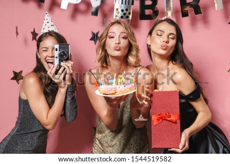 Image of glamour party girls with retro camera holding birthday cake and gift box isolated over pink background