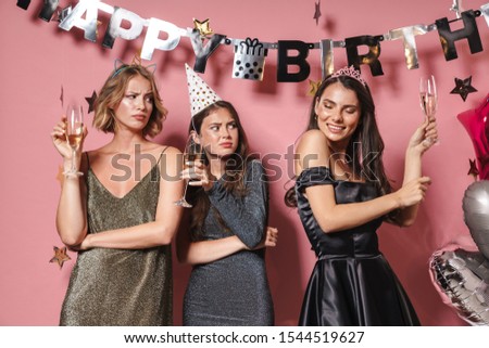 Image of glamour party girls in festive dresses drinking champagne while celebrating birthday isolated over pink background