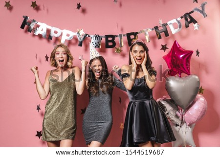 Image of three astonished party girls in festive dresses smiling and celebrating birthday isolated over pink background
