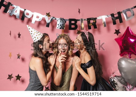 Image of three amazed party girls in festive outfits smiling and celebrating birthday isolated over pink background