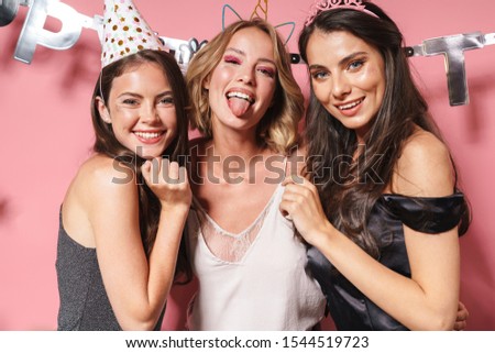 Image of three seductive party girls in festive outfits smiling and celebrating birthday isolated over pink background