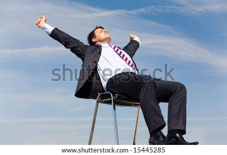 Photo of relaxing businessman sitting on chair and stretching himself on background of blue sky