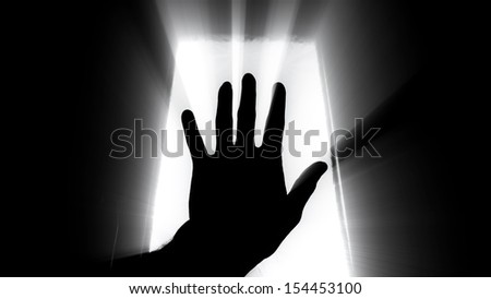 Man's hand held up to the sky with window light and rays of sunshine streaming between the fingers.