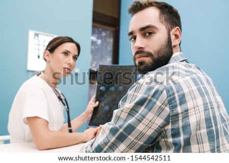 Image of female doctor in medical uniform and serious patient man looking at x-ray scan computed tomography results in hospital